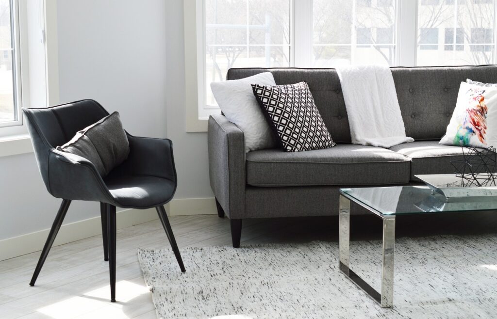 Modern living room with grey sofa, glass table, black chair, and decorative pillows.